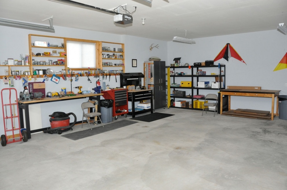 Large garage space with work benches, cabinets for storage and laundry sink.
